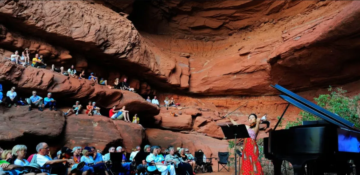 Outdoor patio seating area with fire pit, black chairs around it, picnic tables under a pergola, string lights, and mountains in the background at sunset.