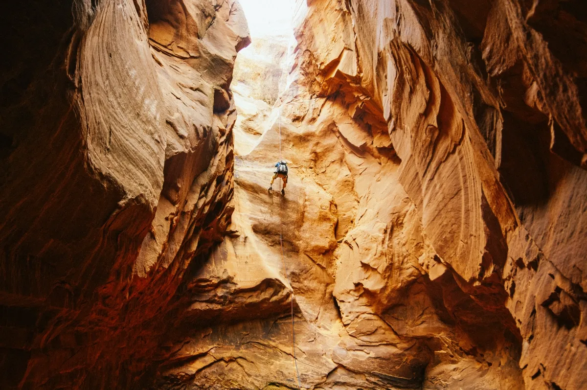 Outdoor patio seating area with fire pit, black chairs around it, picnic tables under a pergola, string lights, and mountains in the background at sunset.