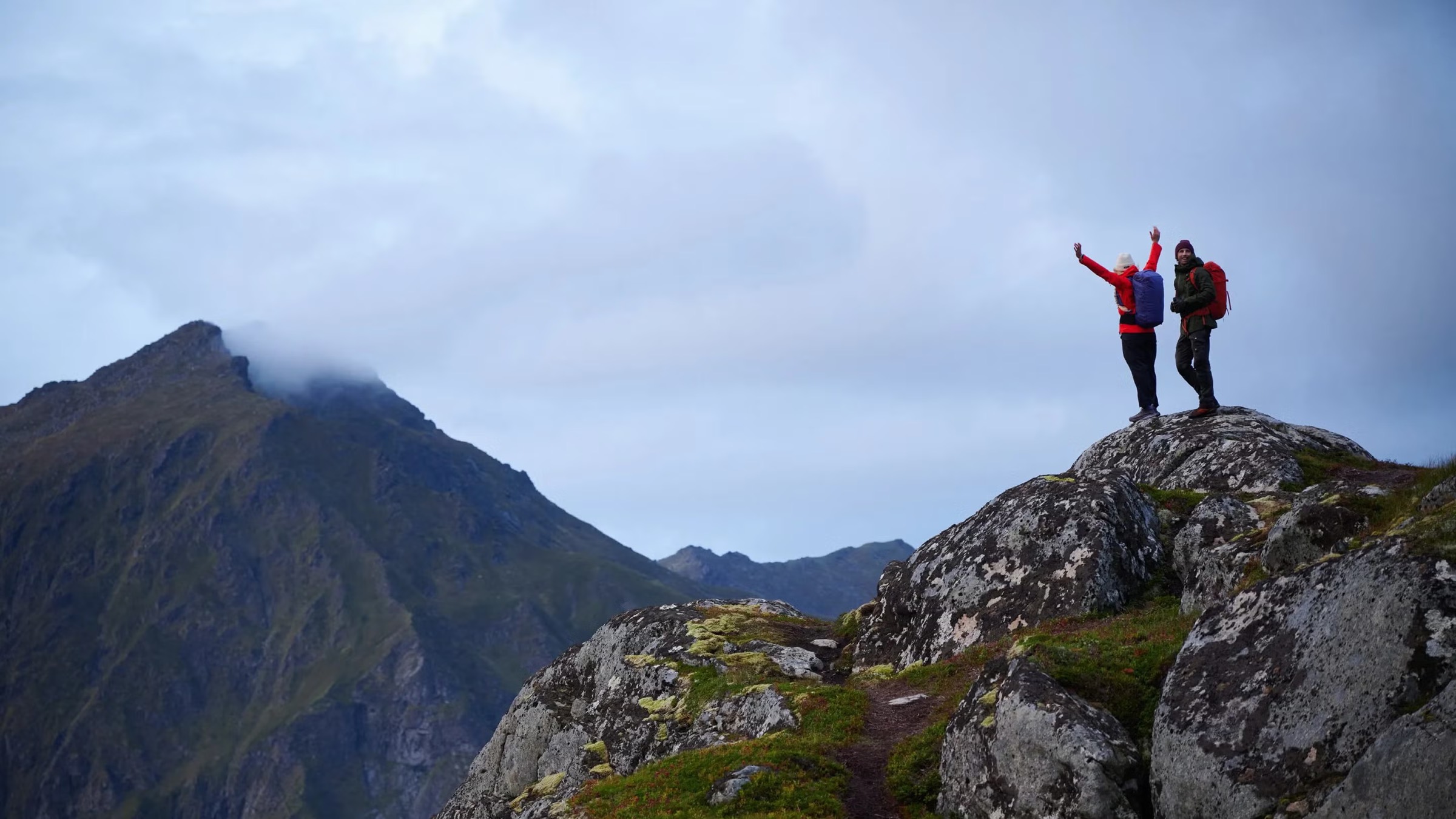 Two hikers in red jackets on a rocky summit above a mountain valley