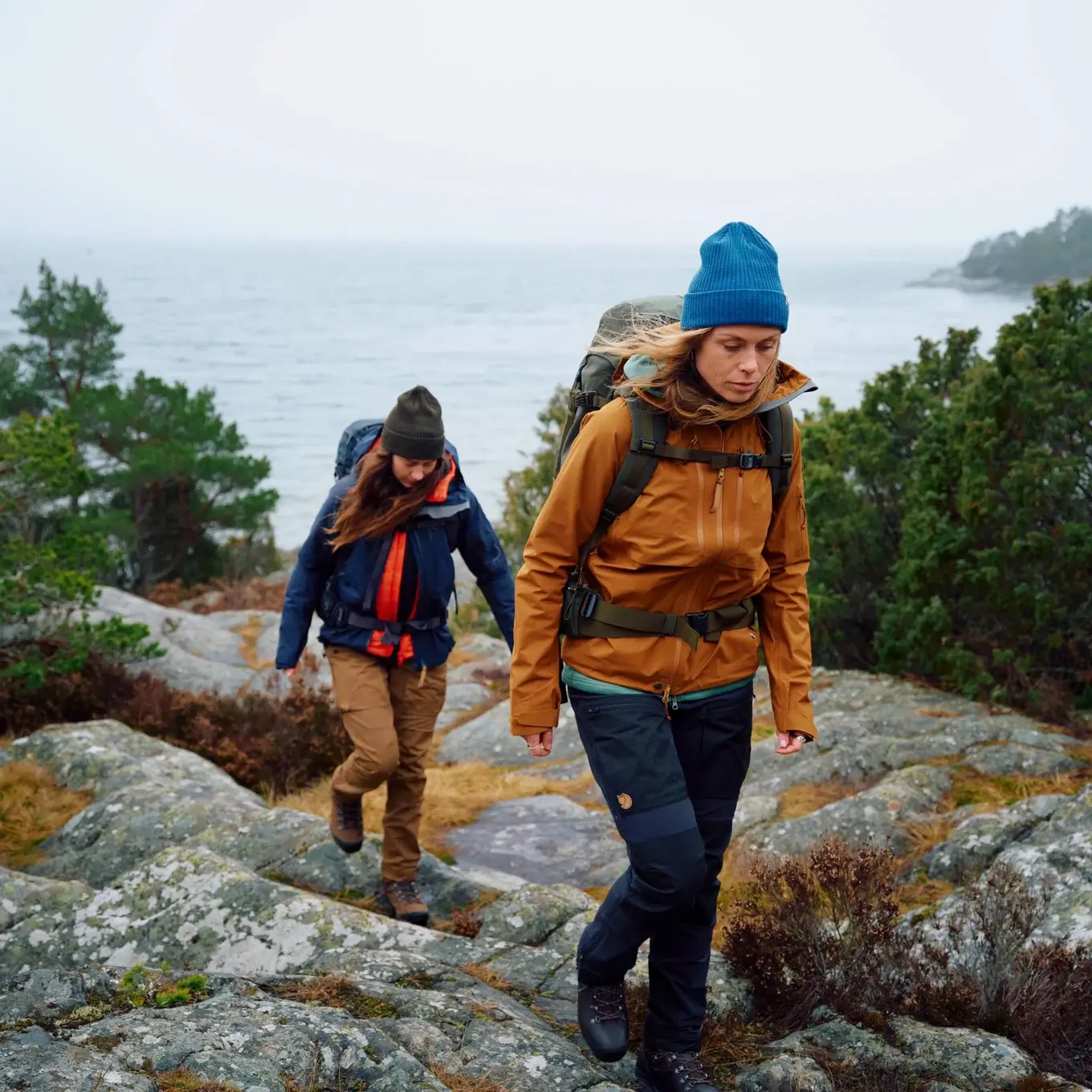 two hikers walking across a rock with large lake in distance