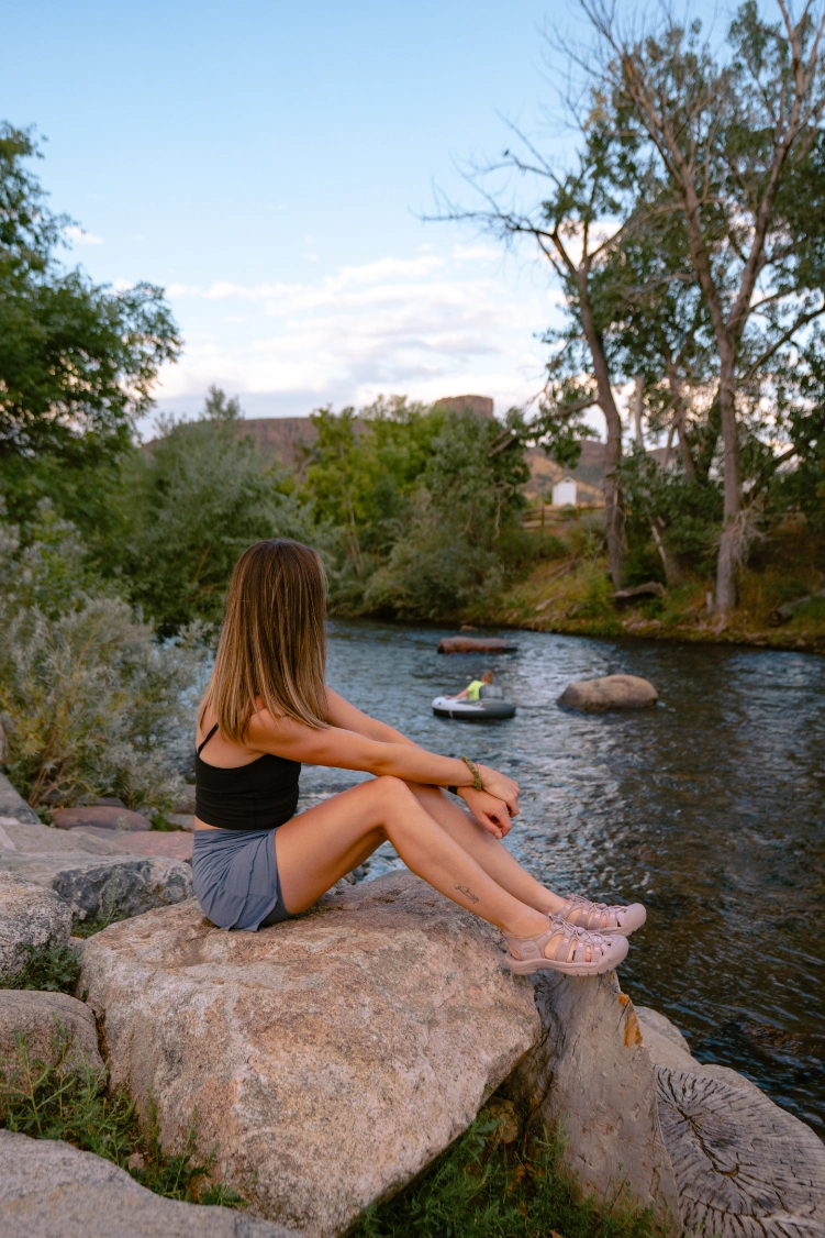 Inflencer sitting on a rock beside a lake wearing KEEN hiking shoes